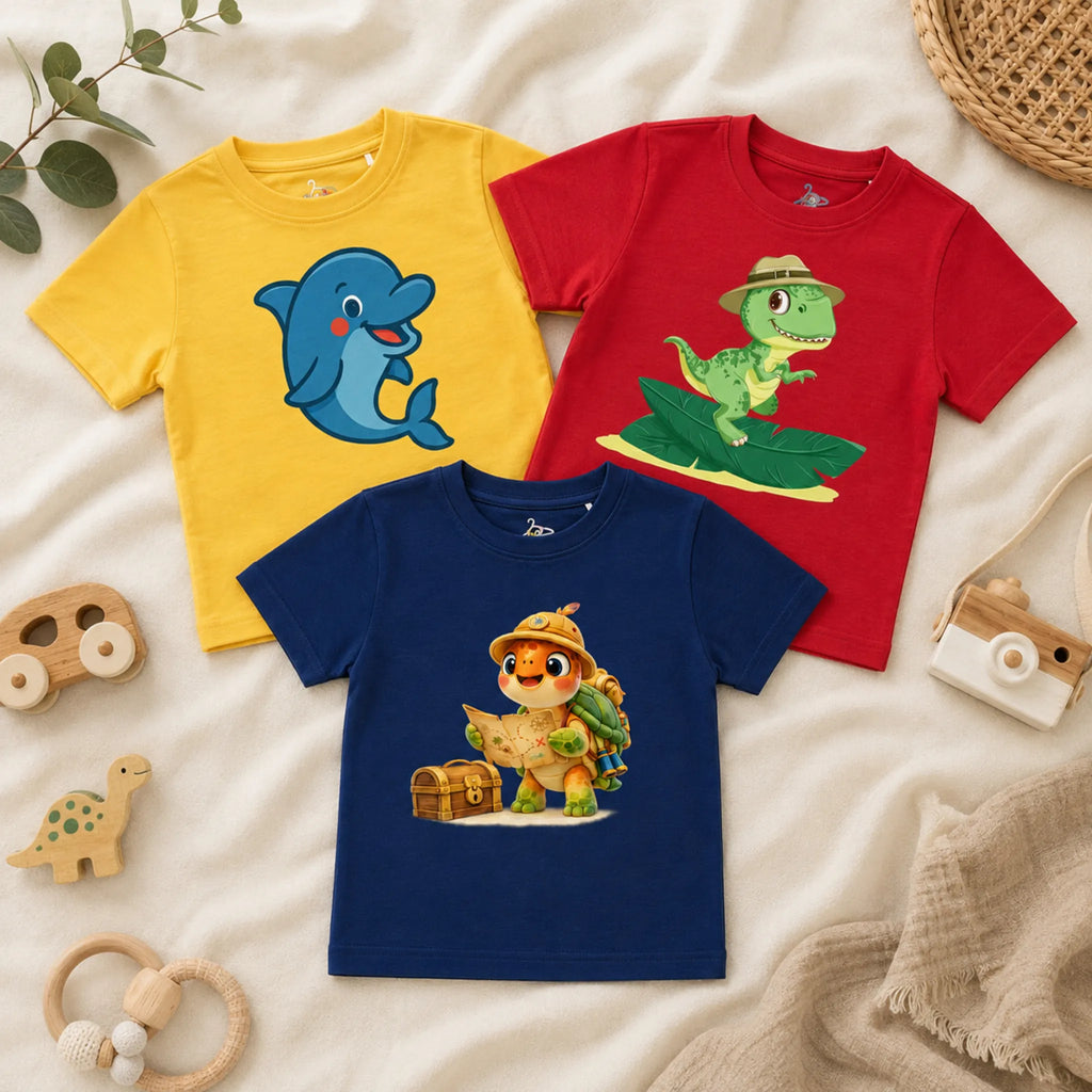 A flatlay of three kid's t-shirts arranged on a textured cream blanket alongside a wooden toy camera, a wooden giraffe, miniature badminton rackets, and woven decor. The shirts include an ivory t-shirt displaying a "FOREST SQUAD" graphic with a bear, fox, raccoon, and rabbit in the woods, a spearmint t-shirt featuring a cheerful purple octopus building a sandcastle, and a lavender t-shirt showing a cute smiling badminton racket hitting a shuttlecock.