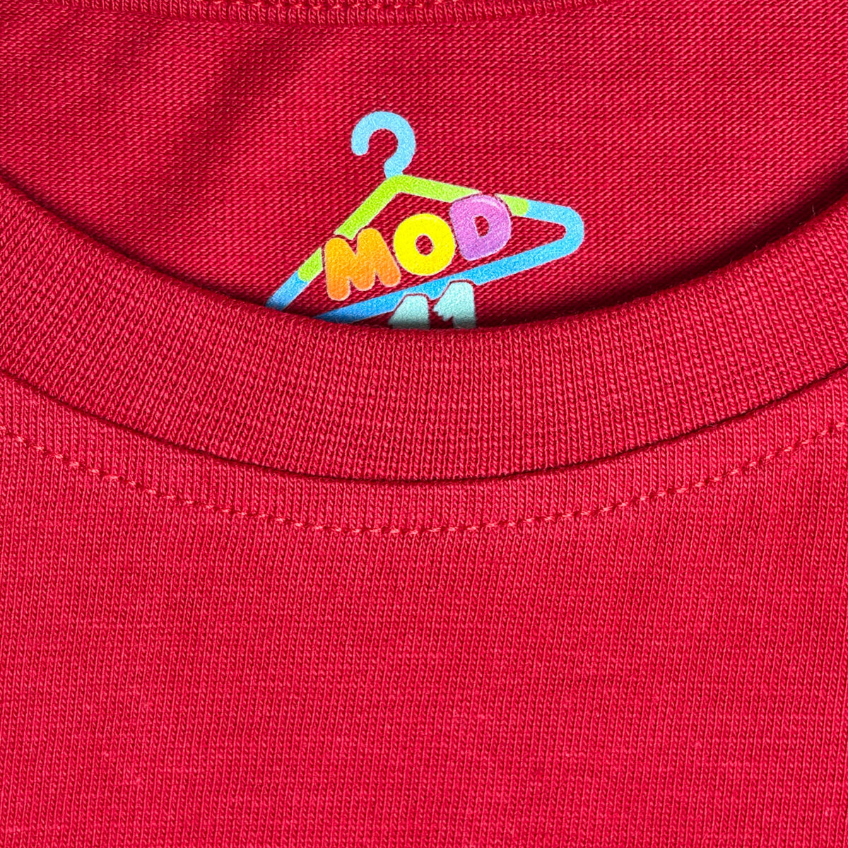 Close-up of a red ribbed knit garment, likely a t-shirt collar, featuring a colorful embroidered logo of a hanger with the letters 'MOD 11' fabric-closeup