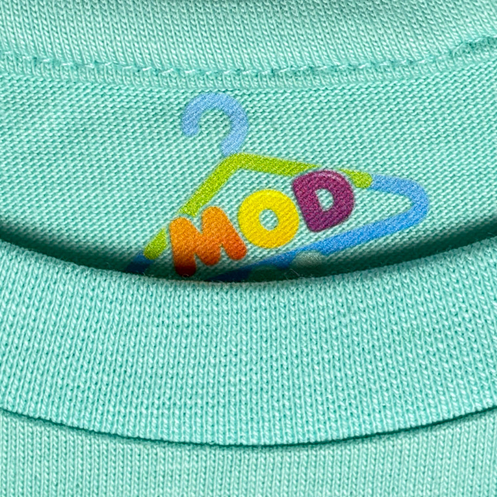Close-up of a mint green knit garment, likely a baby bodysuit or sweater, featuring a colorful embroidered logo of the brand 'MOD 11' on the chest. fabric-closeup